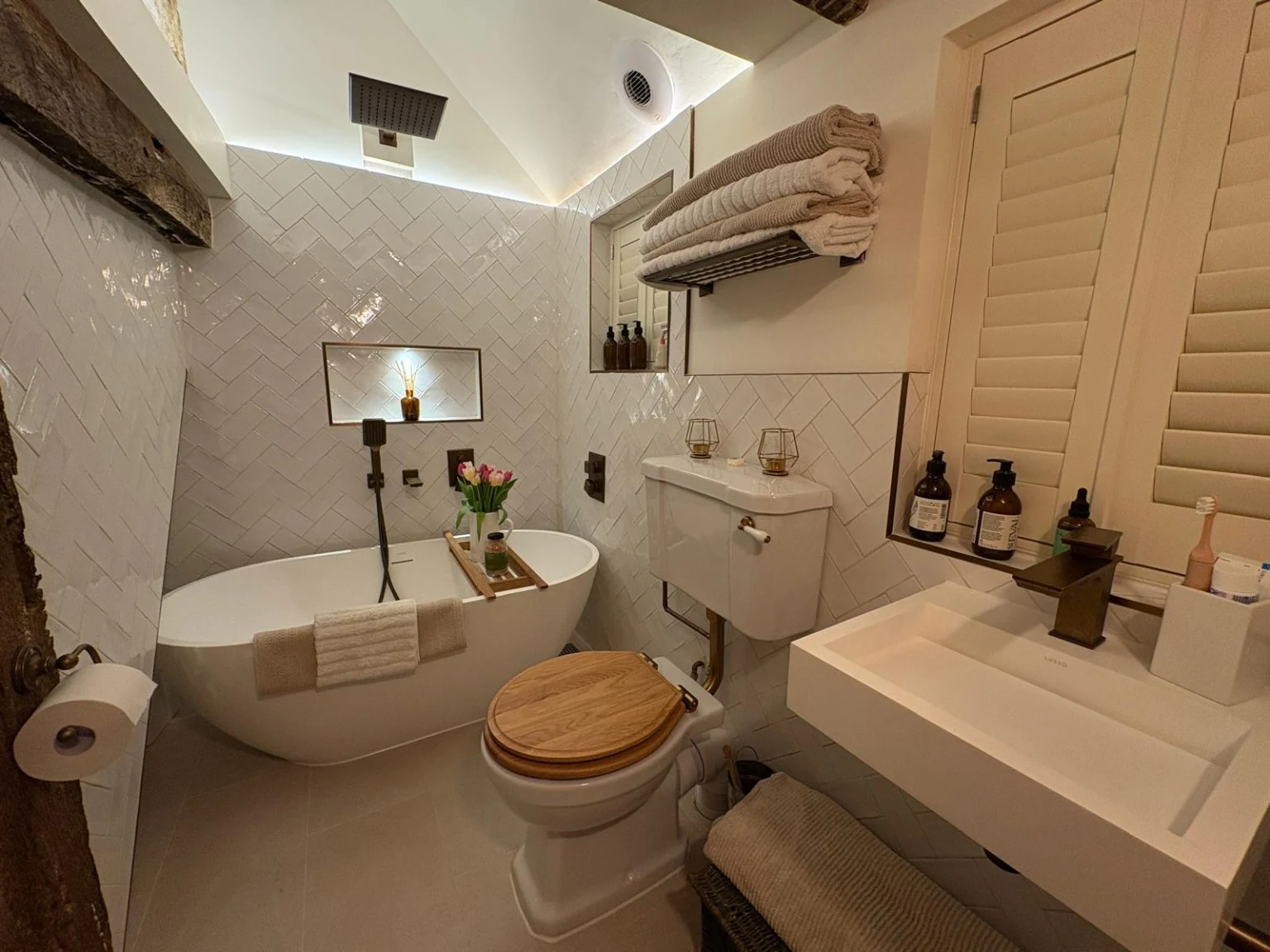 Larger freestanding bath with an overhead shower, no curtain or screen, and an illuminated wall niche