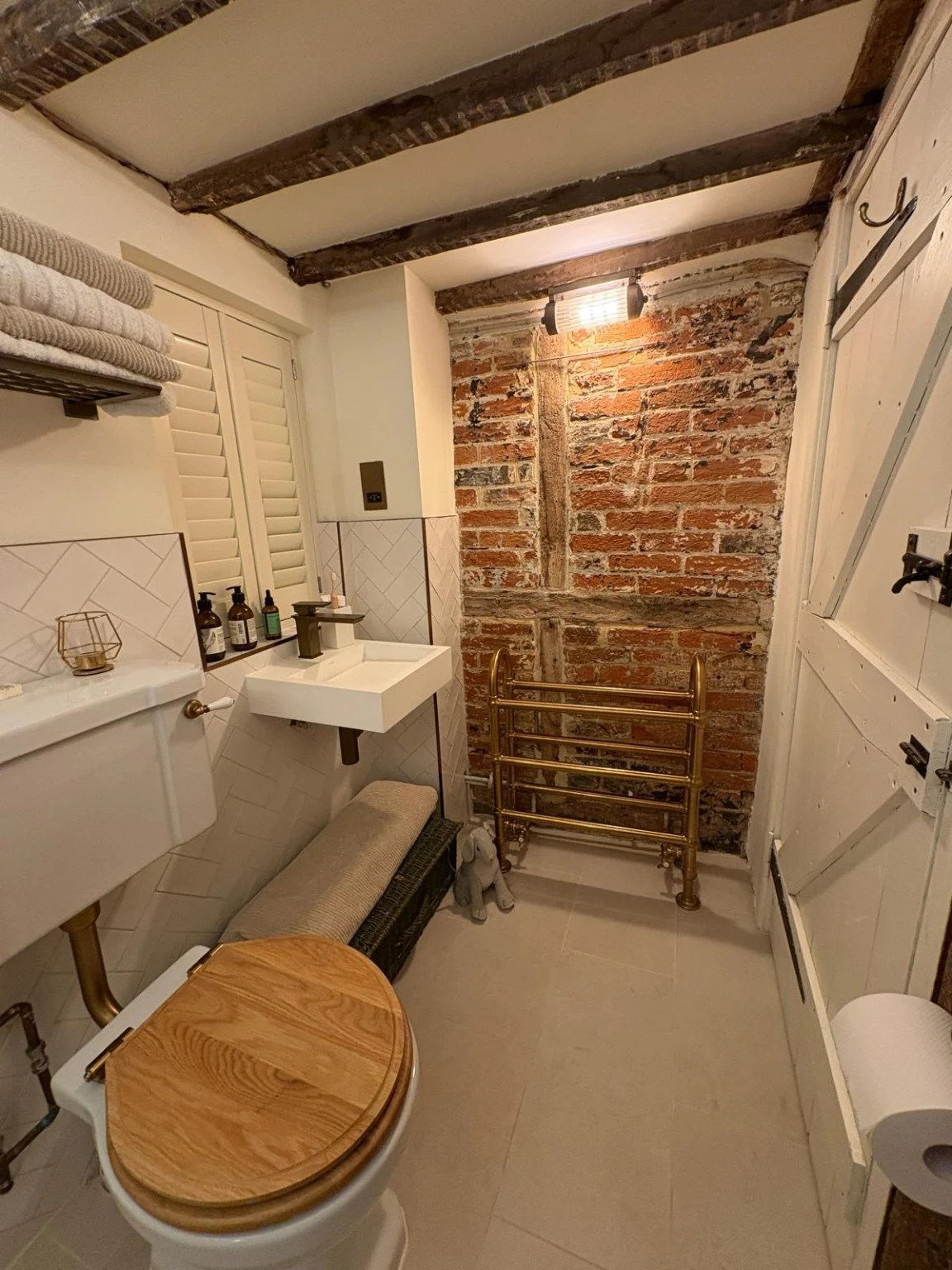 Renovated bathroom with exposed historic brickwork and timber, a towel rail, new lighting and a wall-mounted basin