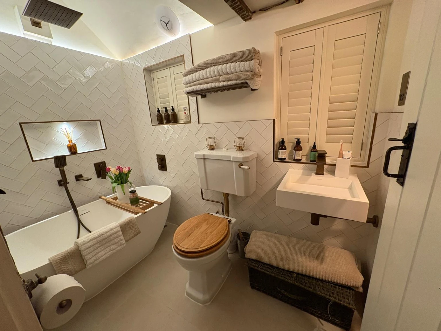 Wide view of the finished bathroom showing the bath, basin, toilet, herringbone wall tiles and tiled floor