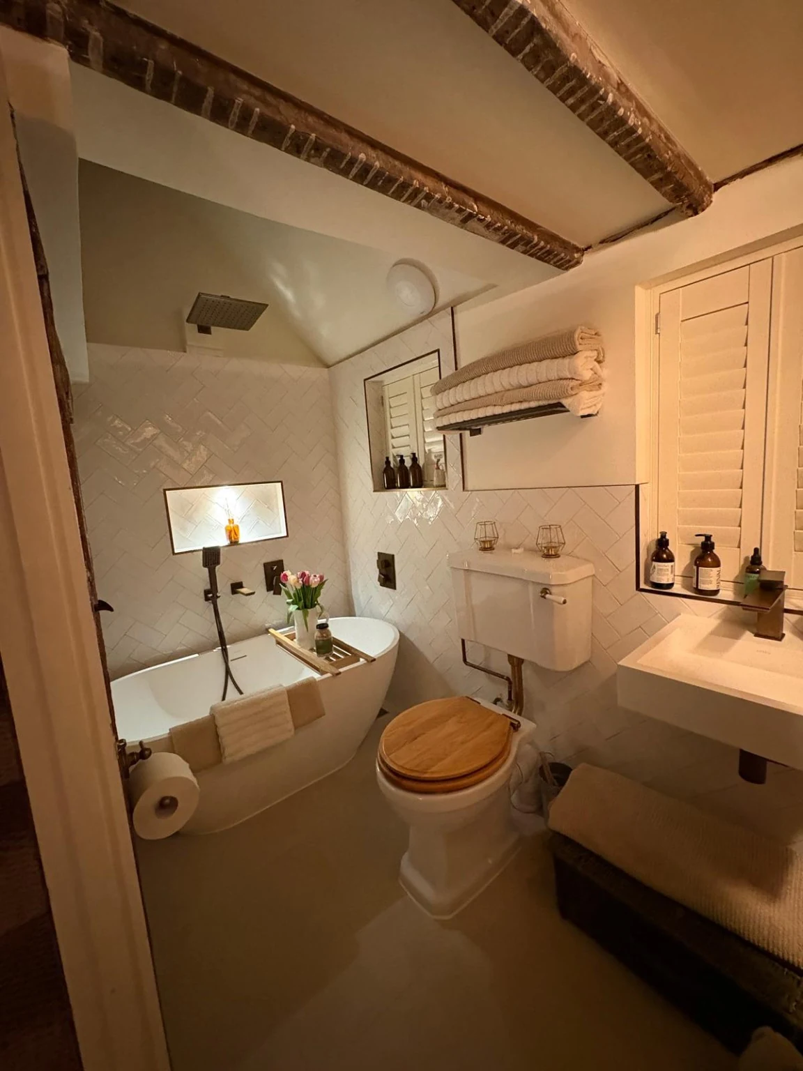 Finished cottage bathroom with a freestanding bath, overhead shower, new basin, toilet and exposed ceiling beams