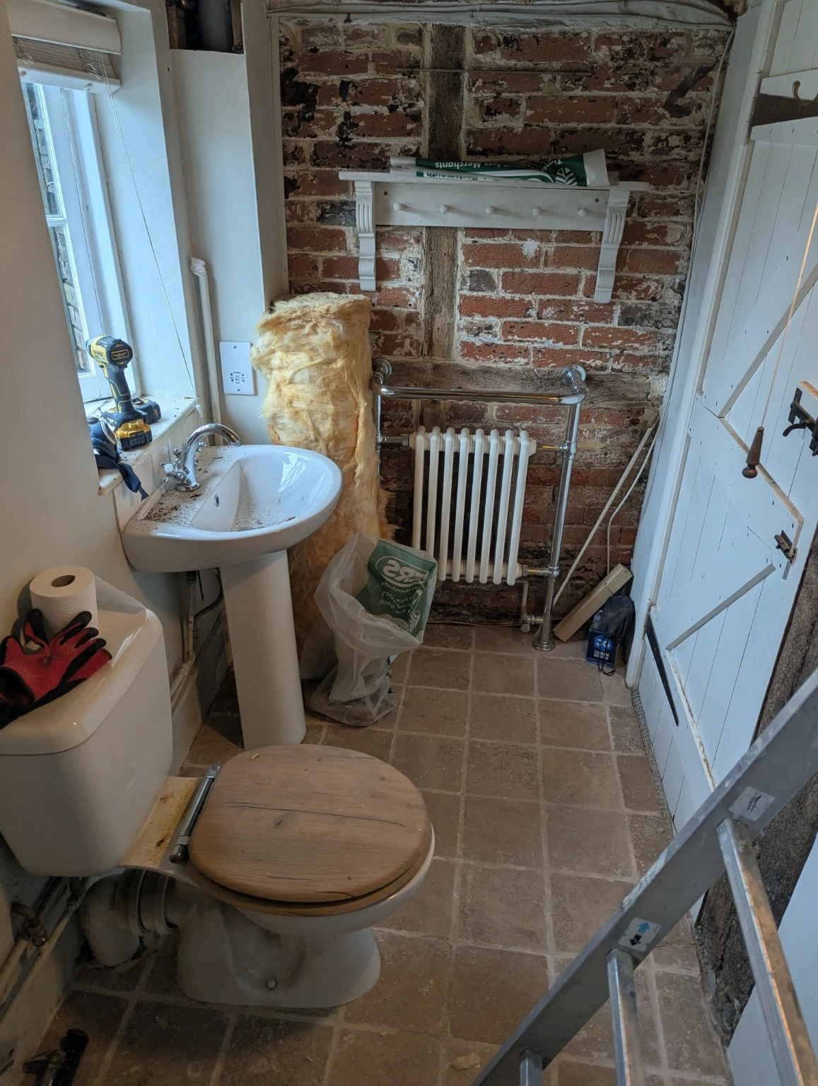 Bathroom during the strip-out, with exposed brick and timber, the old basin and radiator, and tools