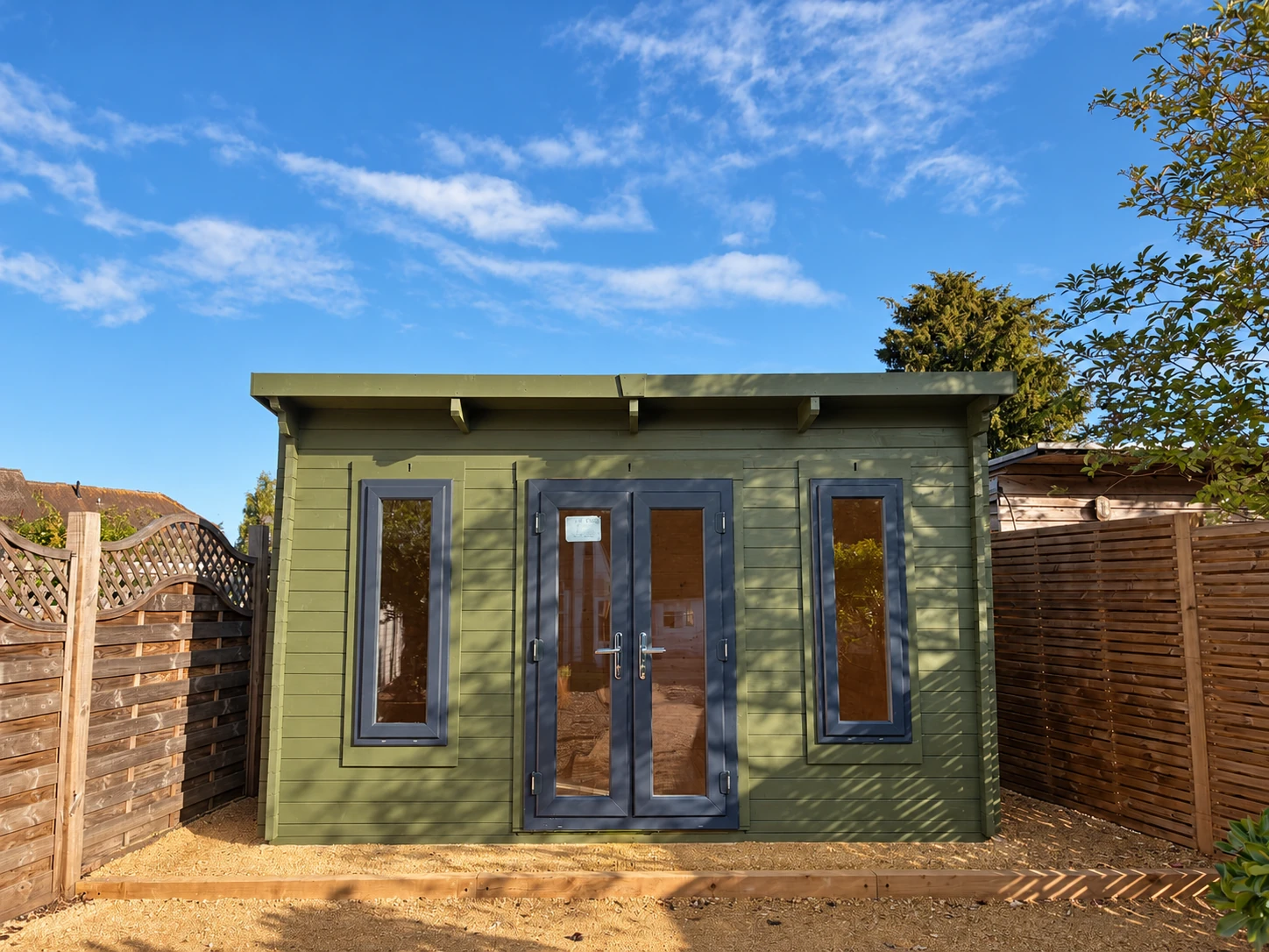 Full front view of the garden room with sunlight and tree shadows across the timber cladding
