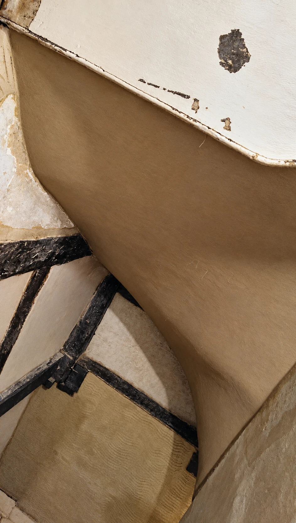 Lime plaster following the curved stairwell alongside exposed historic timber beams